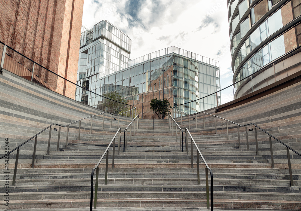 Perspective view of outdoor steps that become walls with stainless steel sleek railings handle grip of leading to entrance into modern building. Geometric shape of concrete staircase, Interesting arch