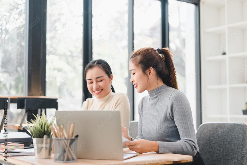 Two women working together on laptop in bright office Two women working together on laptop in bright office