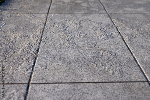 A close-up of grey paving stones covered with patches of ice and frost, emphasizing the slippery and hazardous surface in cold winter conditions. photo