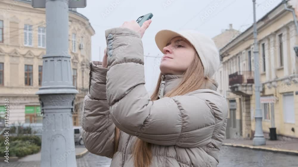 Young woman tourist capturing photos with a smartphone in slow motion while enjoying an urban adventure in winter attire Young woman tourist capturing photos with a smartphone in slow motion while enjoying an urban adventure in winter attire