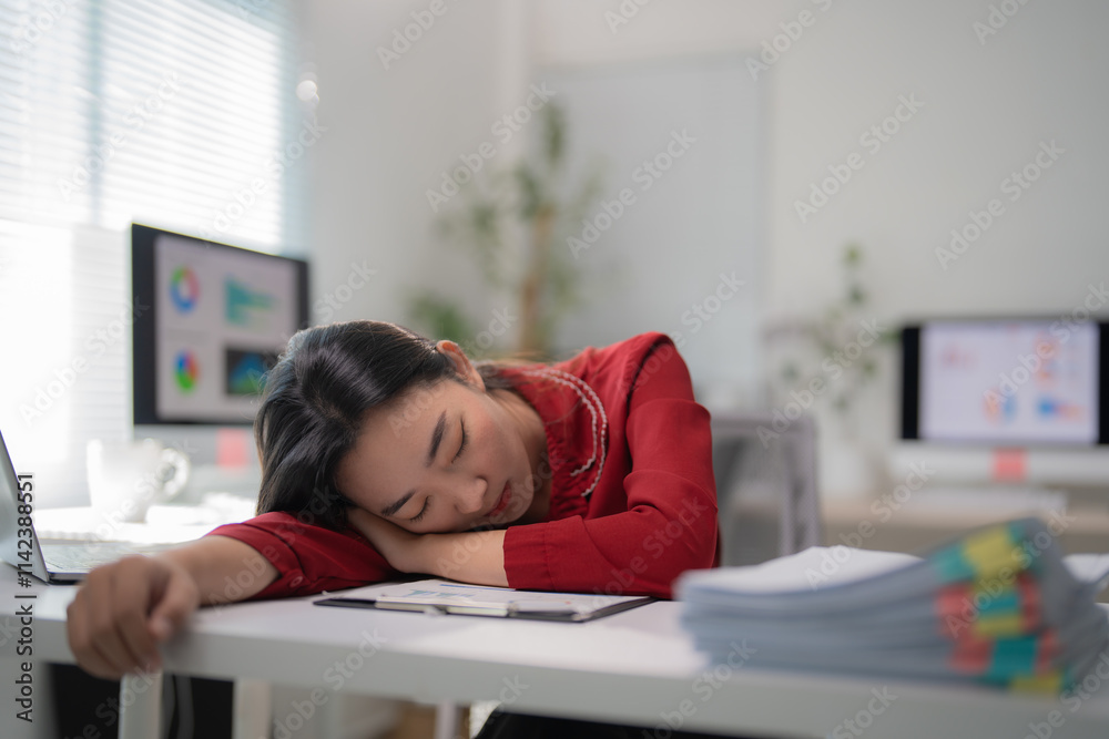 Young office worker sleeping at her desk with documents, laptop and computer on a blurred background, concept of overworked and exhausted employee in the workplace