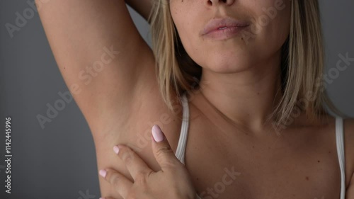 Young blonde woman stroking the armpit showing her perfect smooth skin after depilation on a dark grey background. The result of laser hair removal. Slow motion
