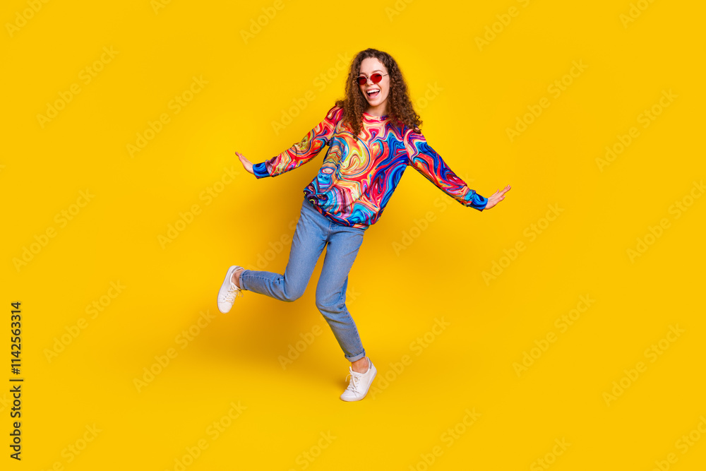 Joyful young woman with curly hair in colorful sweatshirt posing against vibrant yellow background