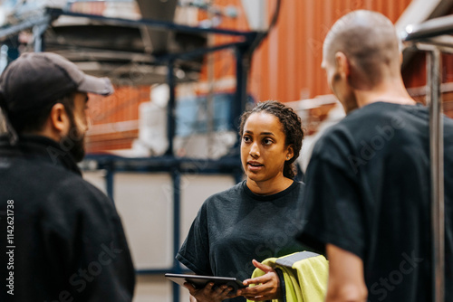 Female warehouse worker holding tablet PC while communicating with male colleagues