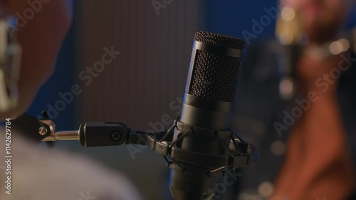 Cropped shot of podcasting process with unrecognizable blurred man and woman engaged in conversation speaking in professional microphone in focus