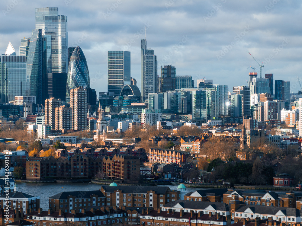 The image captures an aerial view of London's skyline with the Gherkin and modern skyscrapers in Canary Wharf, alongside traditional brick buildings by the Thames.