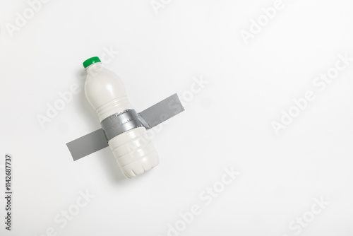 A bottle of milk is attached to a wall using duct tape, presenting an unusual sight. This unexpected display raises curiosity about its purpose and location.