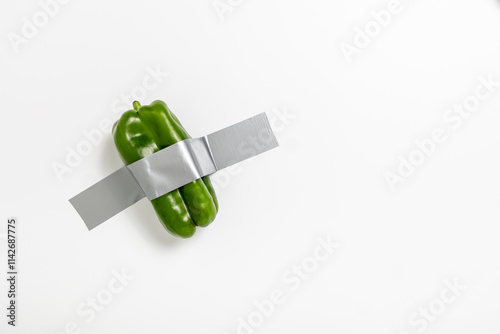 A green pepper is securely attached to a wall using duct tape, showcasing a creative and conceptual approach to integrating food and art. This unusual display invites viewers to ponder its meaning.
