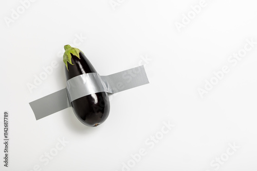 A fresh eggplant is affixed to a plain wall using gray duct tape. This arrangement serves as a unique expression of conceptual art, blending food and unconventional materials into a statement piece.