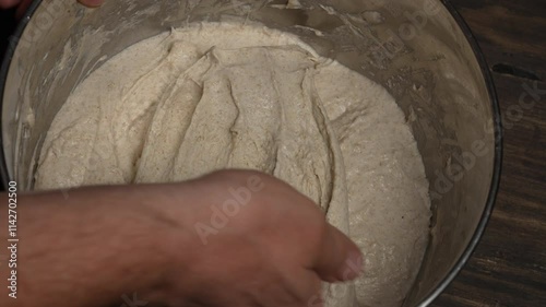 Male baker stretches out yeast-free dough for baking bread with his hands, close up, top view