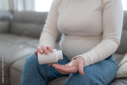 Bild auf Leinwand Unrecognizable pregnant woman holding jar with pills taking vitamins treating sickness during pregnancy sitting on sofa