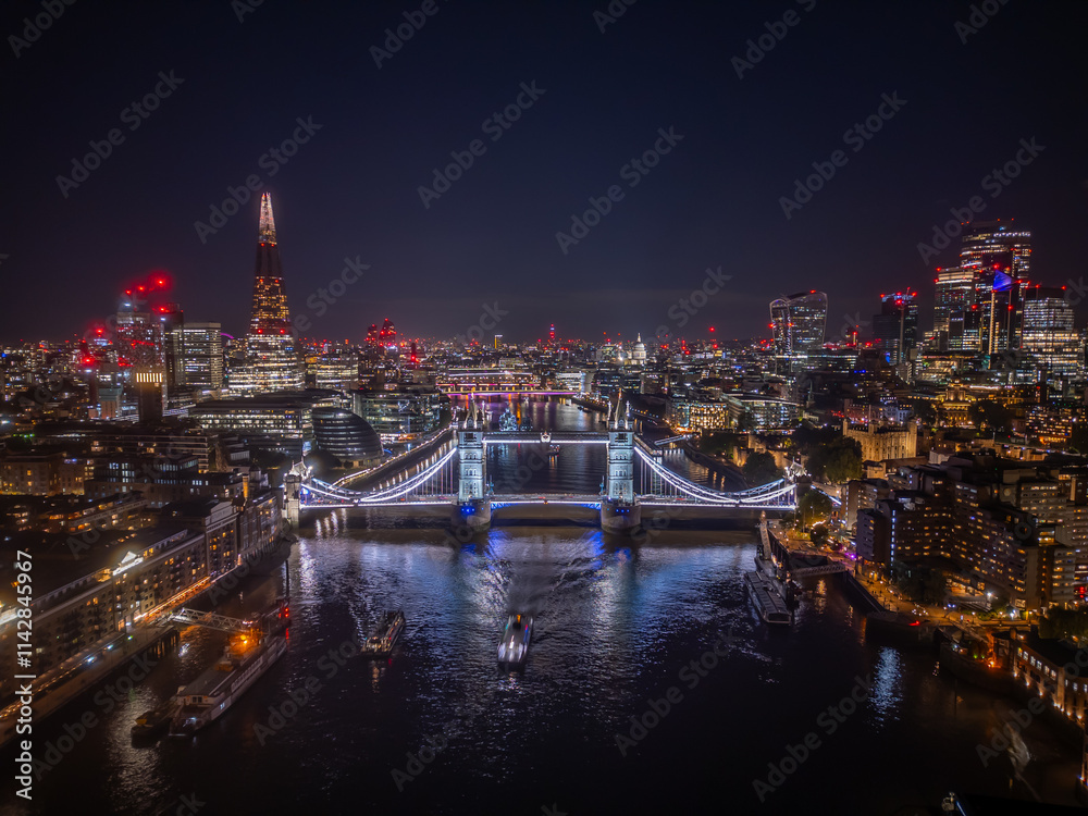 Aerial drone photo of Tower Bridge in London, England, over river Thames at night, with skyscrapers and the lit up city in the background Aerial drone photo of Tower Bridge in London, England, over river Thames at night, with skyscrapers and the lit up city in the background