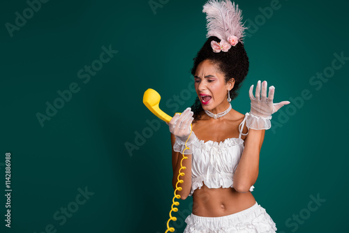 Young woman in an elegant historical costume expresses surprise while holding a retro phone against a green background