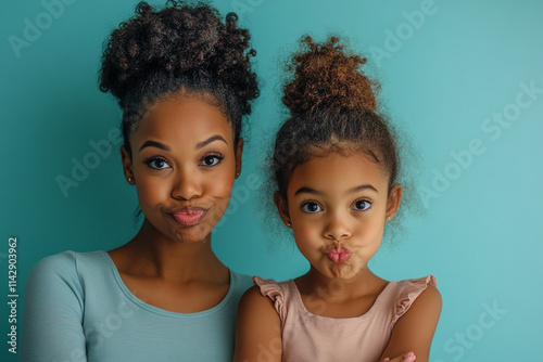 Mother and daughter posing playfully together with funny expressions in front of a blue background