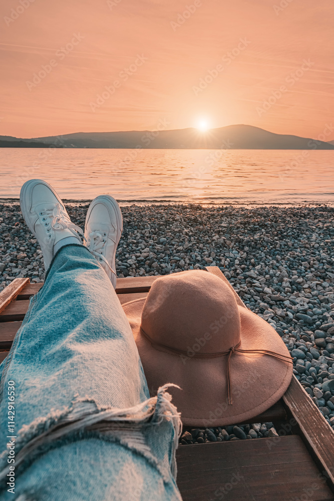 Woman relaxing on deckchair with hat at sunset on pebble beach