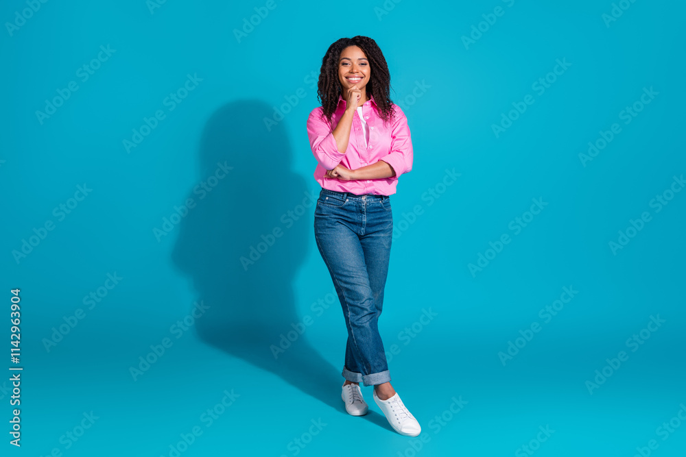 Young woman with stylish curls in a pink shirt stands confidently against a vibrant blue background Young woman with stylish curls in a pink shirt stands confidently against a vibrant blue background