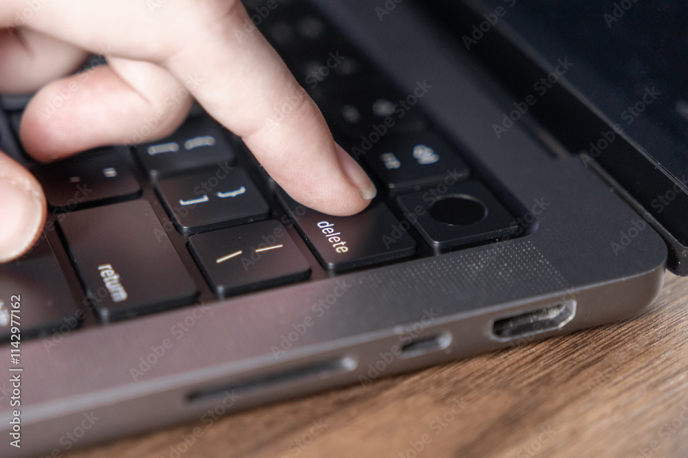 close-up of finger pressing delete key on laptop keyboard with modern design close-up of finger pressing delete key on laptop keyboard with modern design