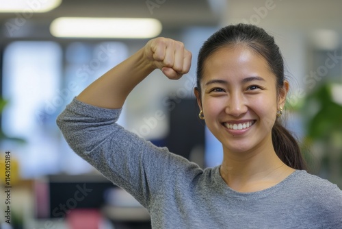 Confident young woman smiling and flexing arm in modern office environment photo