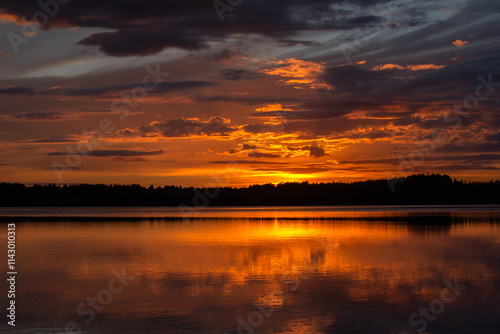 A stunning sunset over a calm lake, with dramatic clouds and warm orange and golden reflections on the water, creating a serene and scenic view.