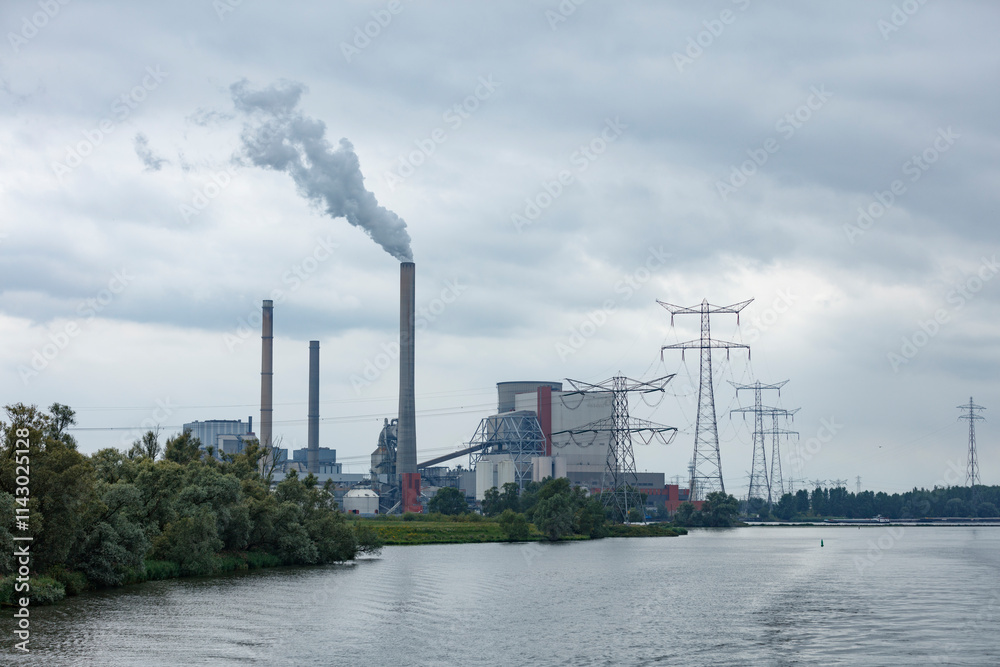 Industrial power plant with smoke stacks and transmission towers by a river. Gray overcast sky. Industrial power plant with smoke stacks and transmission towers by a river. Gray overcast sky.