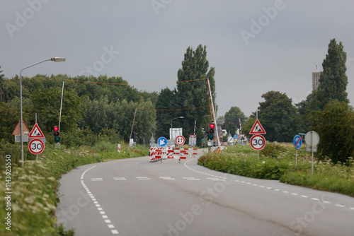 Road closure with temporary barriers and traffic signals.  30 mph speed limit signs visible.  Cloudy day. photo