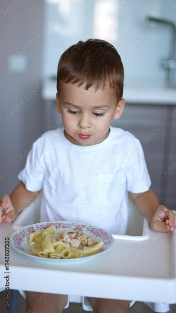 Adorable toddler boy having meals in the kitchen. Cute baby takes a piece from the plate and proposes it to camera. Vertical video. Adorable toddler boy having meals in the kitchen. Cute baby takes a piece from the plate and proposes it to camera. Vertical video.
