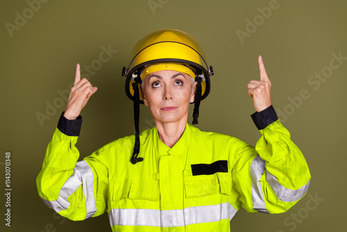 Mature female professional in protective gear pointing upwards, highlighting awareness and focus on safety protocols. photo