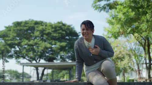 CaregiverWoman in Gray Cardigan Sitting Outdoors in Distress, Holding Her Chest with Concern for Health Amidst Natures Greenery in Park photo