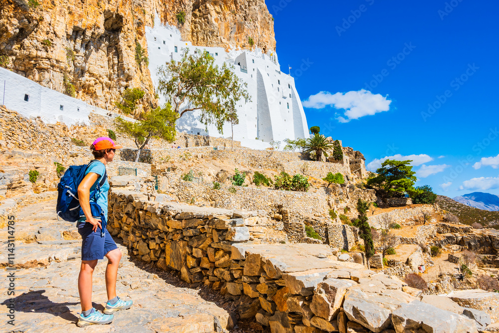 Woman tourist with backpack trekking to Panagia Hozoviotissa monastery and looking at sea coast, Amorgos island, Cyclades, Greece