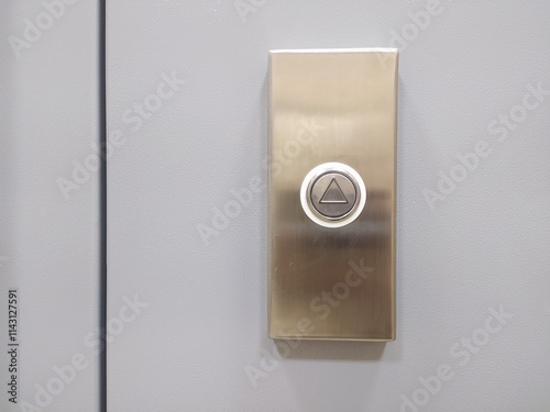 Elevator call button with up arrow on grey wall.