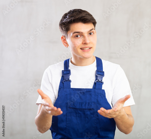 Young experienced worker in jumpsuit is actively gesticulating,pointing hands to side and inviting to see something.Man points to chest with hand and draws attention of listeners to his speech photo