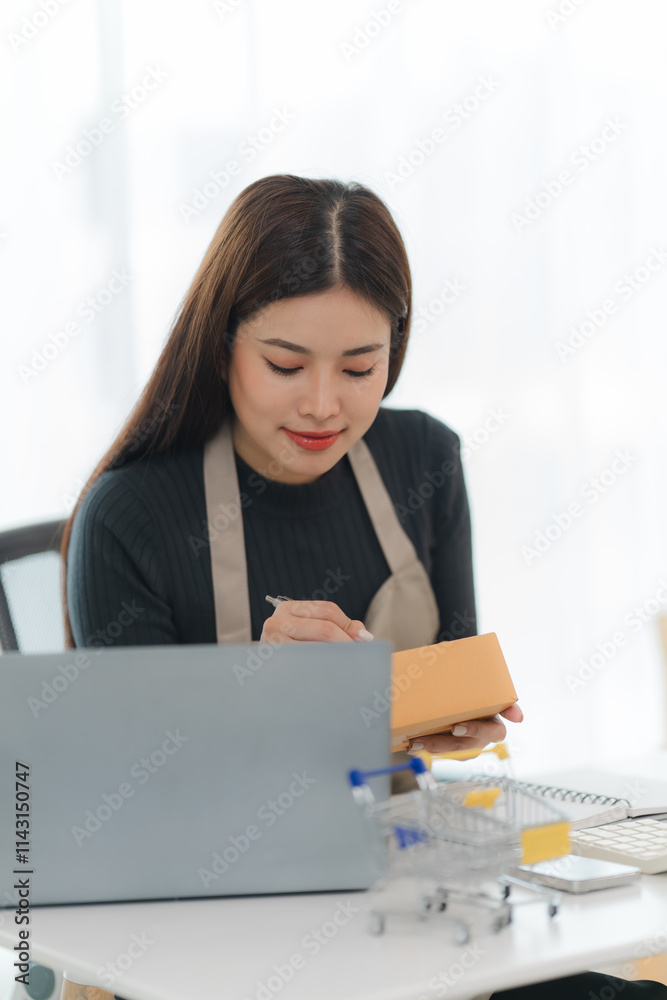 Small Business Owner Processing Orders: A young woman in an apron diligently works on her laptop, fulfilling orders. The image captures the dedication and hard work of small business owners. Small Business Owner Processing Orders: A young woman in an apron diligently works on her laptop, fulfilling orders. The image captures the dedication and hard work of small business owners.