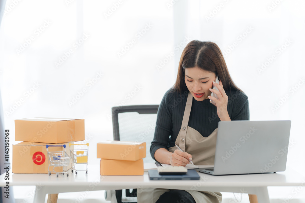 Focused Online Business Owner: A young Asian woman, dressed in an apron, efficiently manages her online business. She's on a phone call, taking notes, with several parcels on her desk. Focused Online Business Owner: A young Asian woman, dressed in an apron, efficiently manages her online business. She's on a phone call, taking notes, with several parcels on her desk.