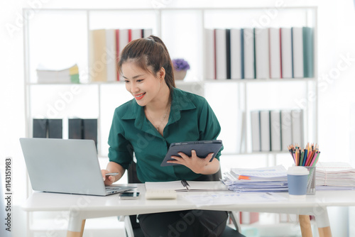 Focused and Efficient: Young businesswoman working productively at her desk with laptop and tablet, surrounded by organized paperwork and supplies. photo