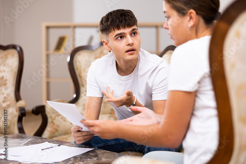 Young married couple is sitting at a desk in an apartment, carefully studying important documents photo