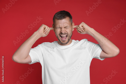 Man covering his ears with fingers on red background