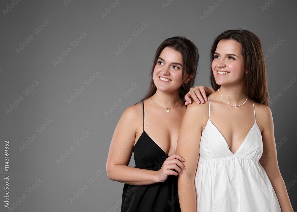 Portrait of beautiful twin sisters on grey background, space for text Portrait of beautiful twin sisters on grey background, space for text