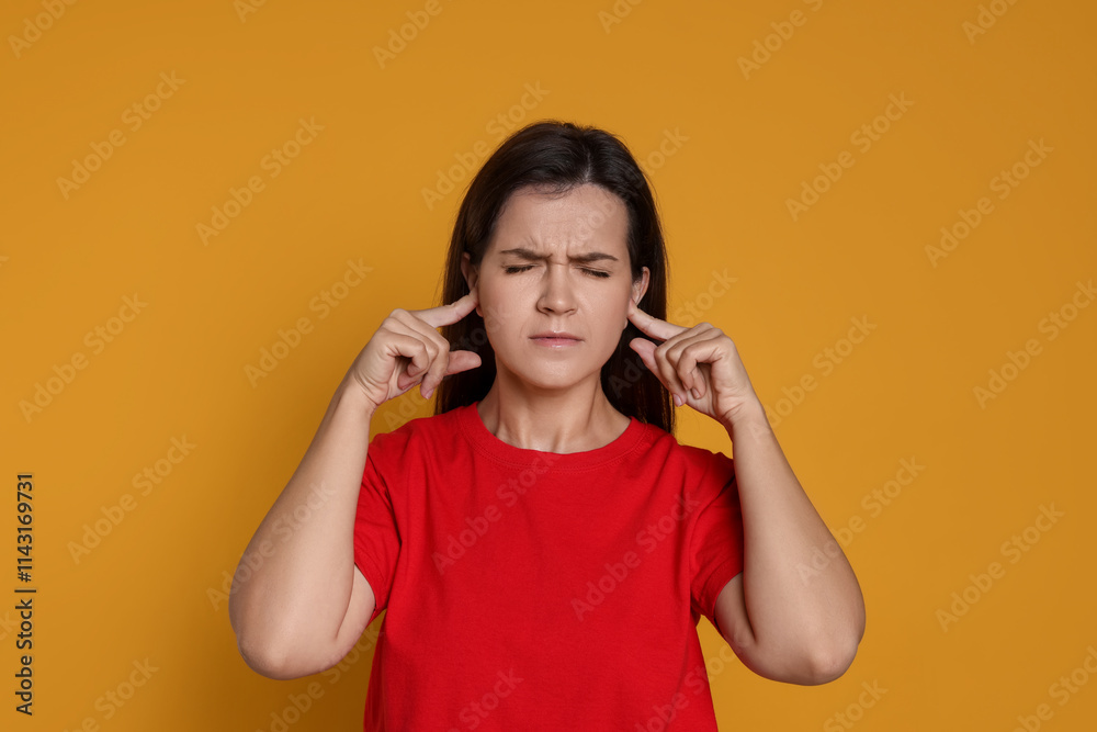 Woman covering her ears with fingers on orange background Woman covering her ears with fingers on orange background