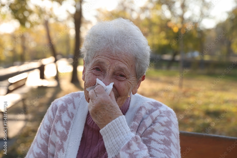 Senior woman with tissue blowing runny nose in park