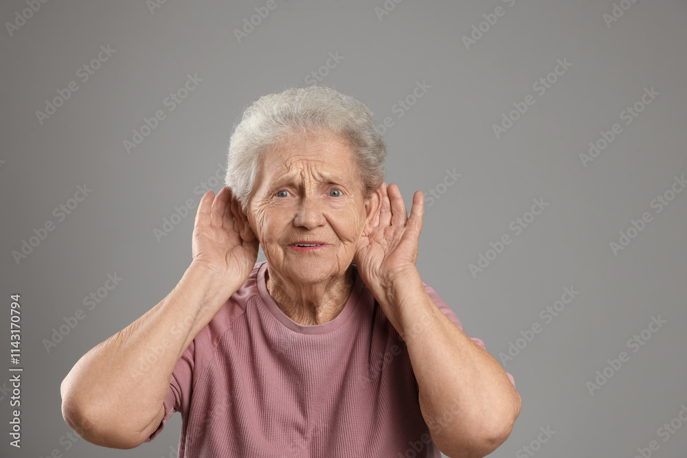 Senior woman showing hand to ear gesture on grey background Senior woman showing hand to ear gesture on grey background