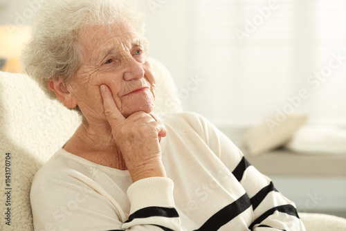 Pensive senior woman sitting on armchair at home