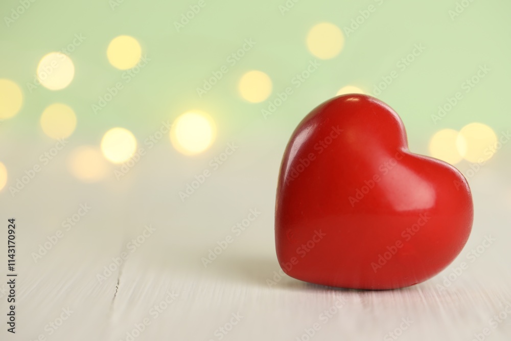 Fototapeta premium Red heart on white wooden table against festive lights, space for text. St. Valentine's day