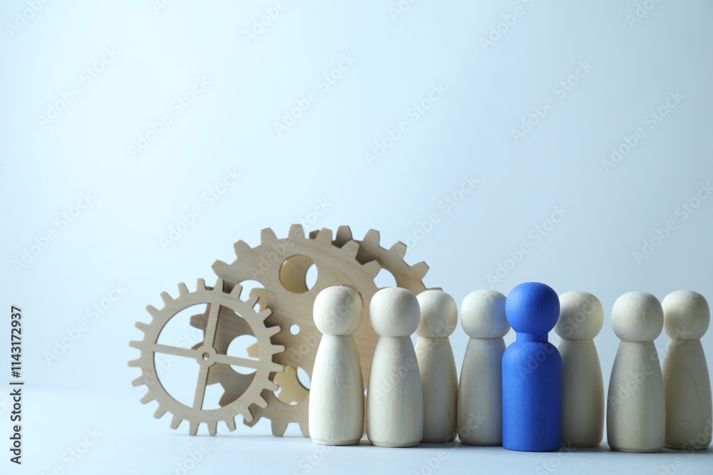 Human resources concept. Blue figure among wooden ones and gearwheels on light background, closeup. Space for text Human resources concept. Blue figure among wooden ones and gearwheels on light background, closeup. Space for text