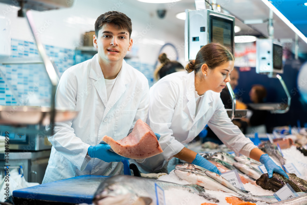 Obraz premium Male seller demonstrates large piece of tuna fillet at the fish market