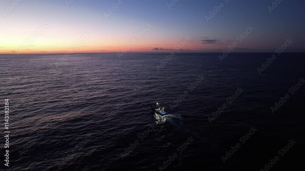 Imagem de um atuneiro navegando tranquilamente nas águas do Oceano Atlântico, com o sol nascente iluminando o horizonte.