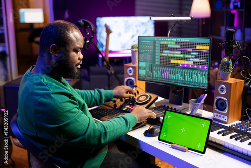 Confident musician producing tracks on mixing console in home studio, using isolated mockup screen and editing music in post production. Artist performer creating new beats for his songs.