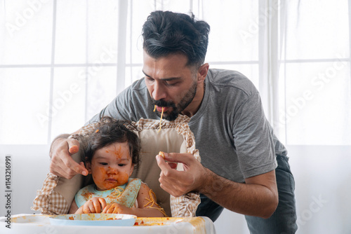 Handsome young man feeding spaghetti healthy daughter messy sitting on high chair at home. Dirty innocence infant girl hungry eating spaghetti with fatherhood single care in room. Lifestyle family.