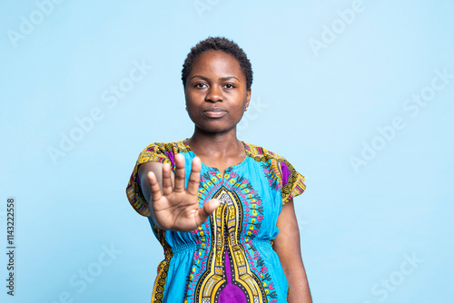 African american serious woman showing stop sign with her palm, expressing refusal and negativity. Young adult raising hand and presenting rejection, angry displeased girl in studio. photo