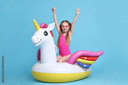 Valokuva Happy little girl in beachwear with inflatable unicorn shaped ring on light blue