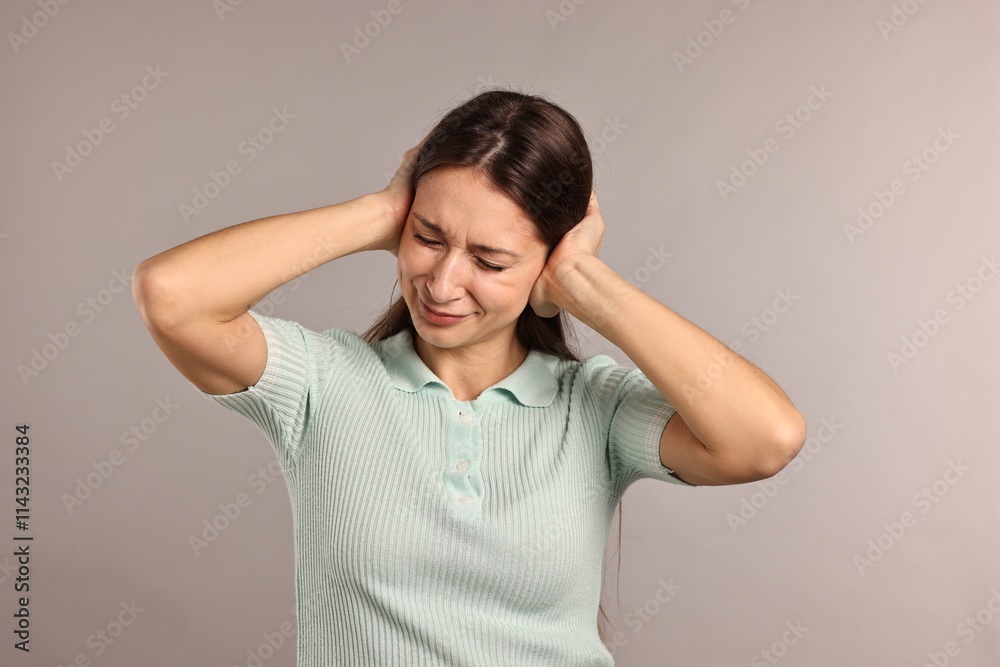 Annoyed woman covering her ears due to loud sound on light grey background Annoyed woman covering her ears due to loud sound on light grey background